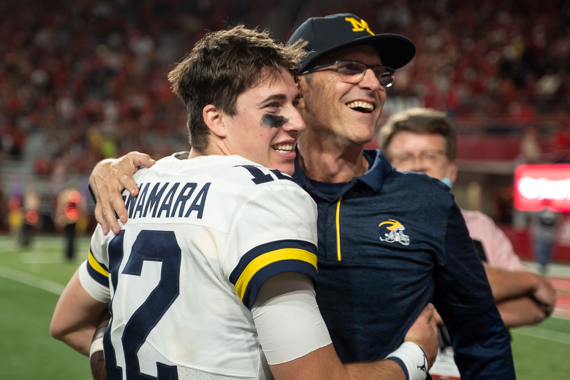 Michigan coach Jim Harbaugh on the left hugs Michigan quarterback Cade McNamara after a victory