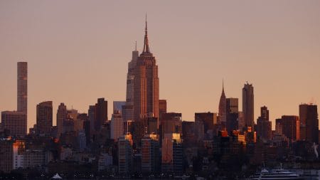 The sun rises behind the skyline of midtown Manhattan, the Empire State Building, One Vanderbilt and the Chrysler Building in New York City