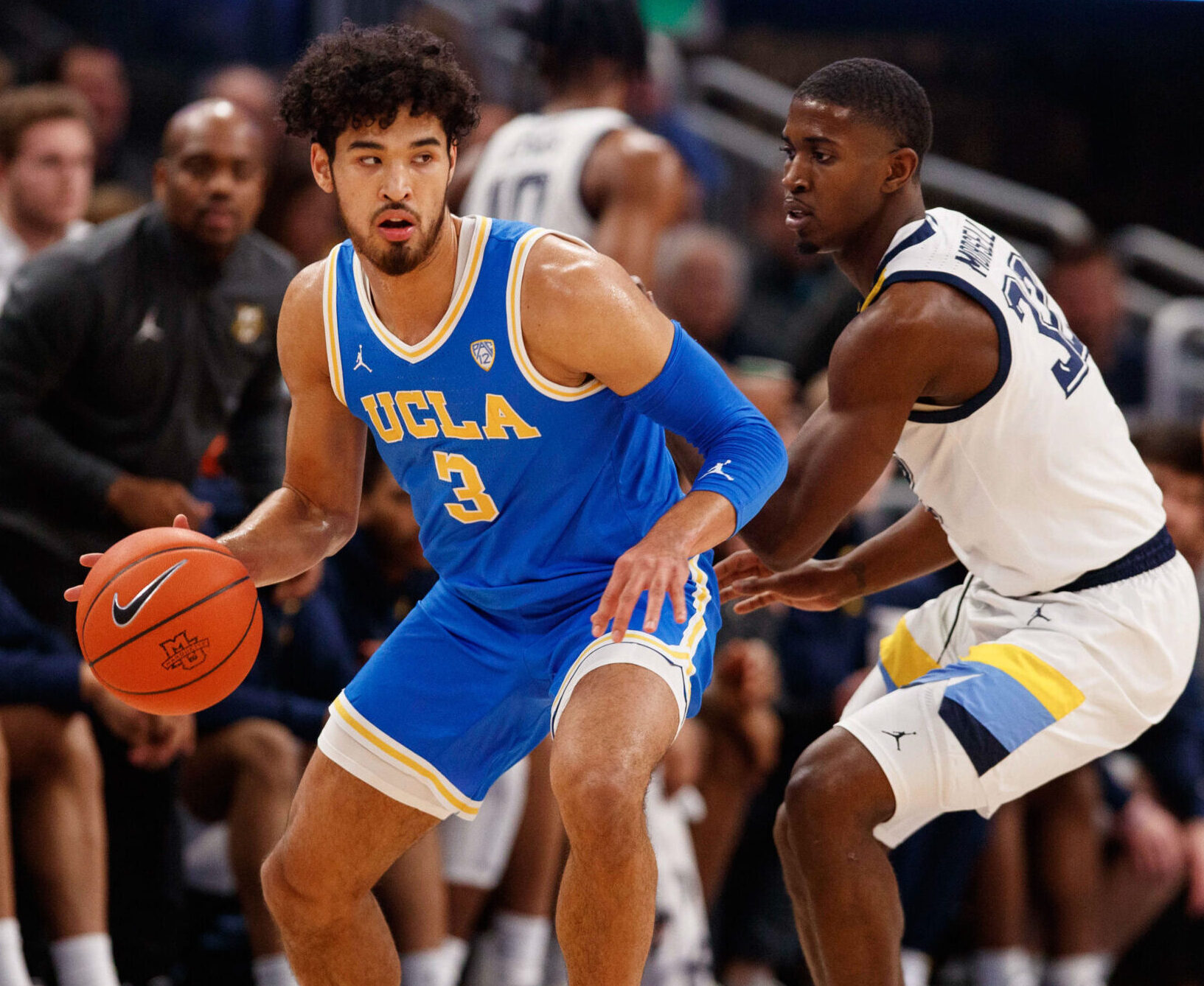 UCLA Bruins guard Johnny Juzang (left) dribbles the basketball during agame against the Marquette Golden Eagles