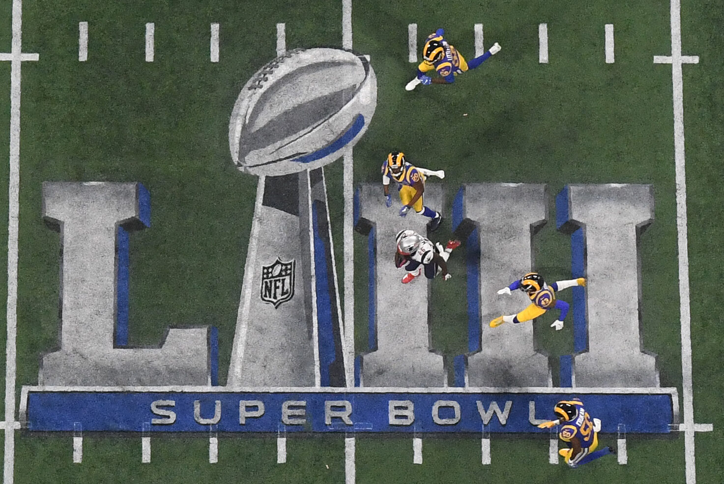 On overhead photo of New England Patriots running back Sony Michel carrying the ball while running over the Super Bowl 53 logo against the Los Angeles Rams in Super Bowl 53