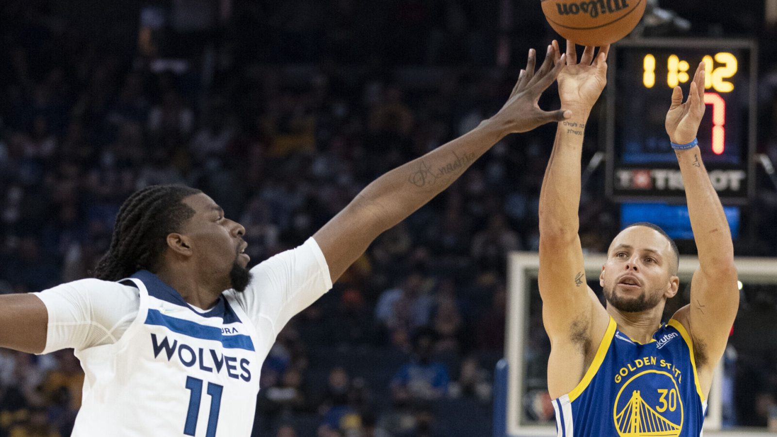 Golden State Warriors guard Stephen Curry (right) shoots the basketball over the outstretched left hand of Minnesota Timberwolves center Naz Reid (left)