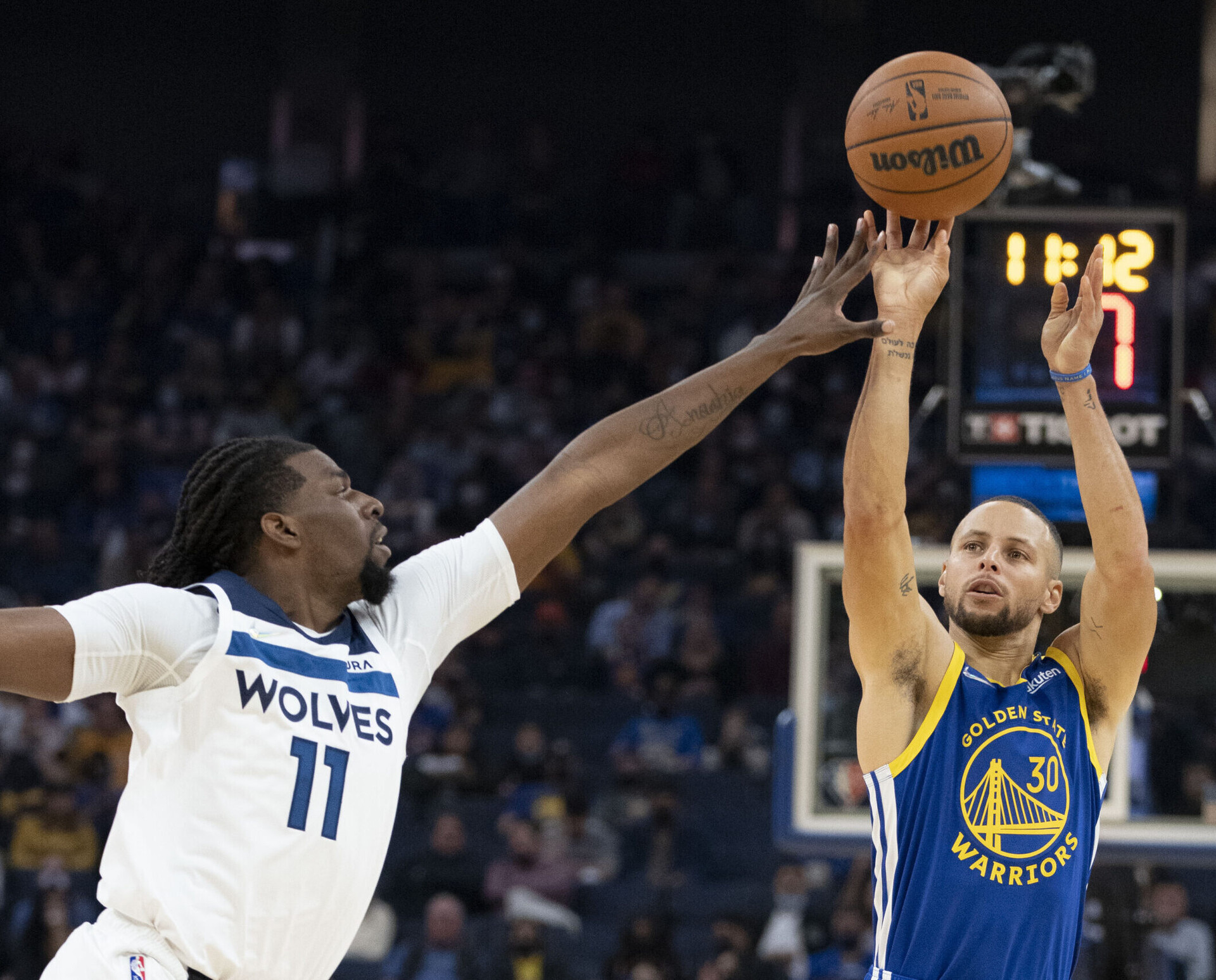 Golden State Warriors guard Stephen Curry (right) shoots the basketball over the outstretched left hand of Minnesota Timberwolves center Naz Reid (left)
