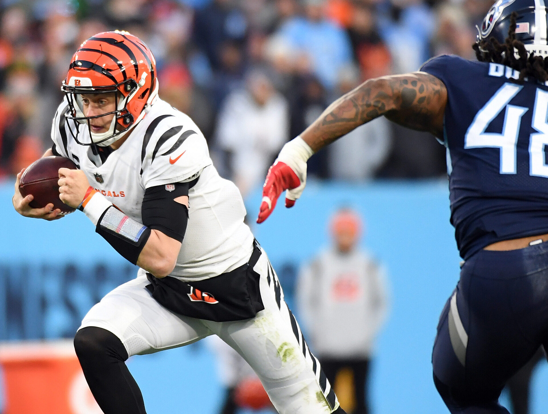 Cincinnati Bengals quarterback Joe Burrow (left) runs the football while being pursued by Tennessee Titans outside linebacker Bud Dupree (right)