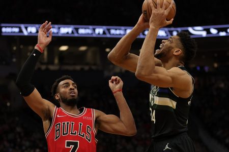 Milwaukee Bucks forward Giannis Antetokounmpo (right) holds the ball above his head while being guarded by the Chicago Bulls' Troy Brown Jr. (left)