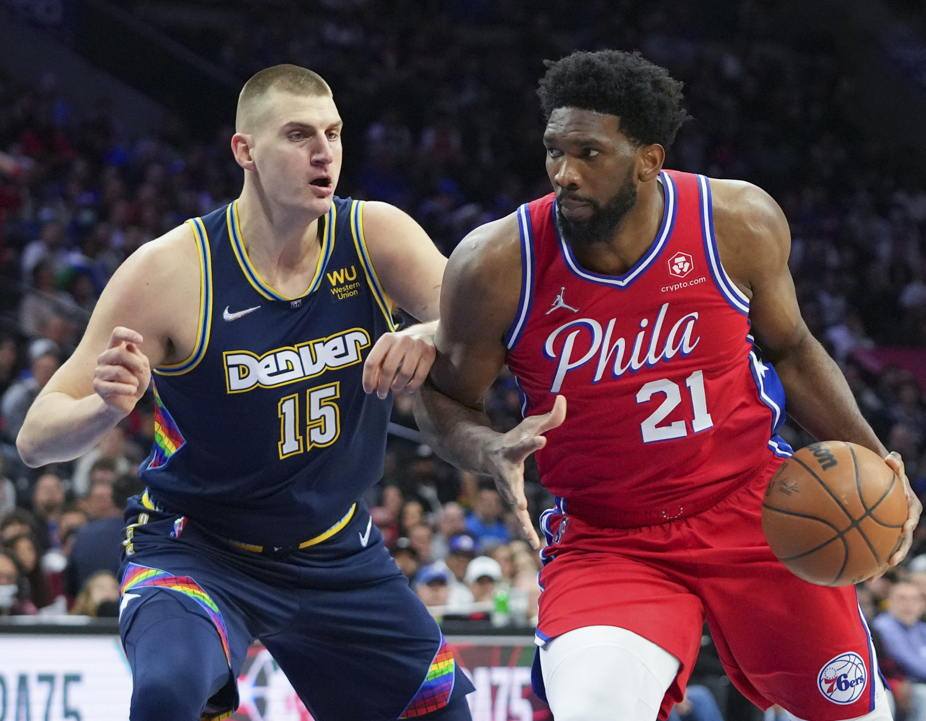 Joel Embiid (right) dribbles the basketball with his left hand while defending Denver Nuggets center Nikola Jokic (left) uses his left forearm to keep Embiid from driving to the basket