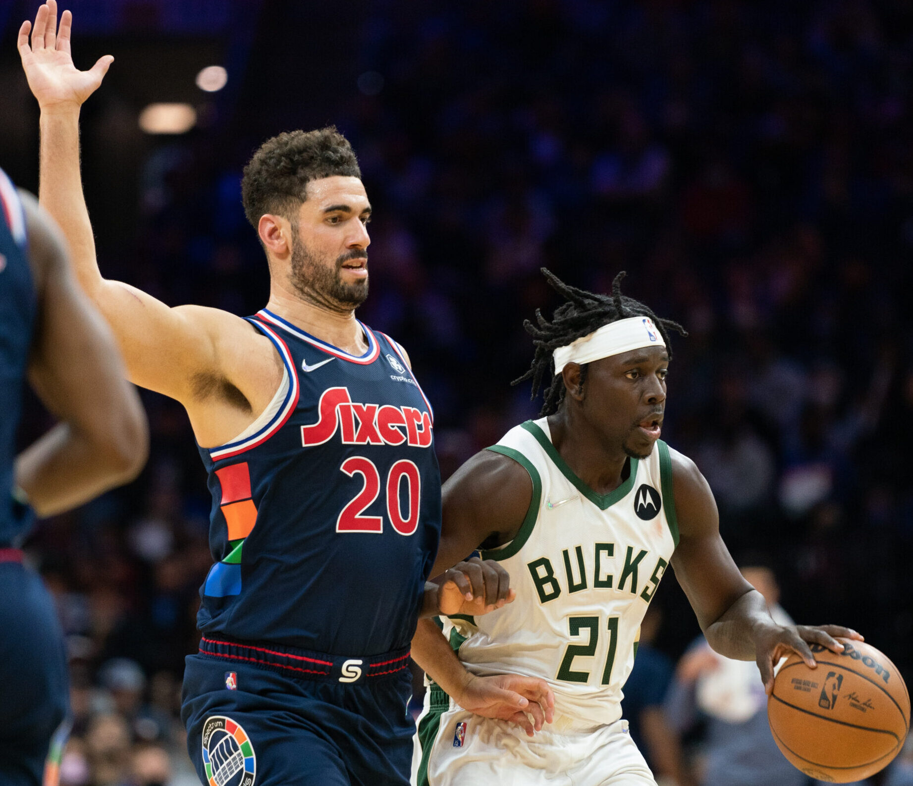 Milwaukee Bucks guard Jrue Holiday (right) dribbles the ball while Philadelphia 76ers forward Georges Niang (left) raises his right arm and applies defensive pressure