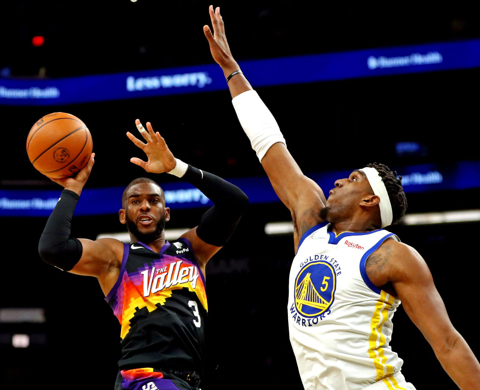 Phoenix Suns guard Chris Paul (left) jumps and prepares to pass the basketball with his right hand while Golden State Warriors center Kevon Looney (right) defends with his outstretched right arm