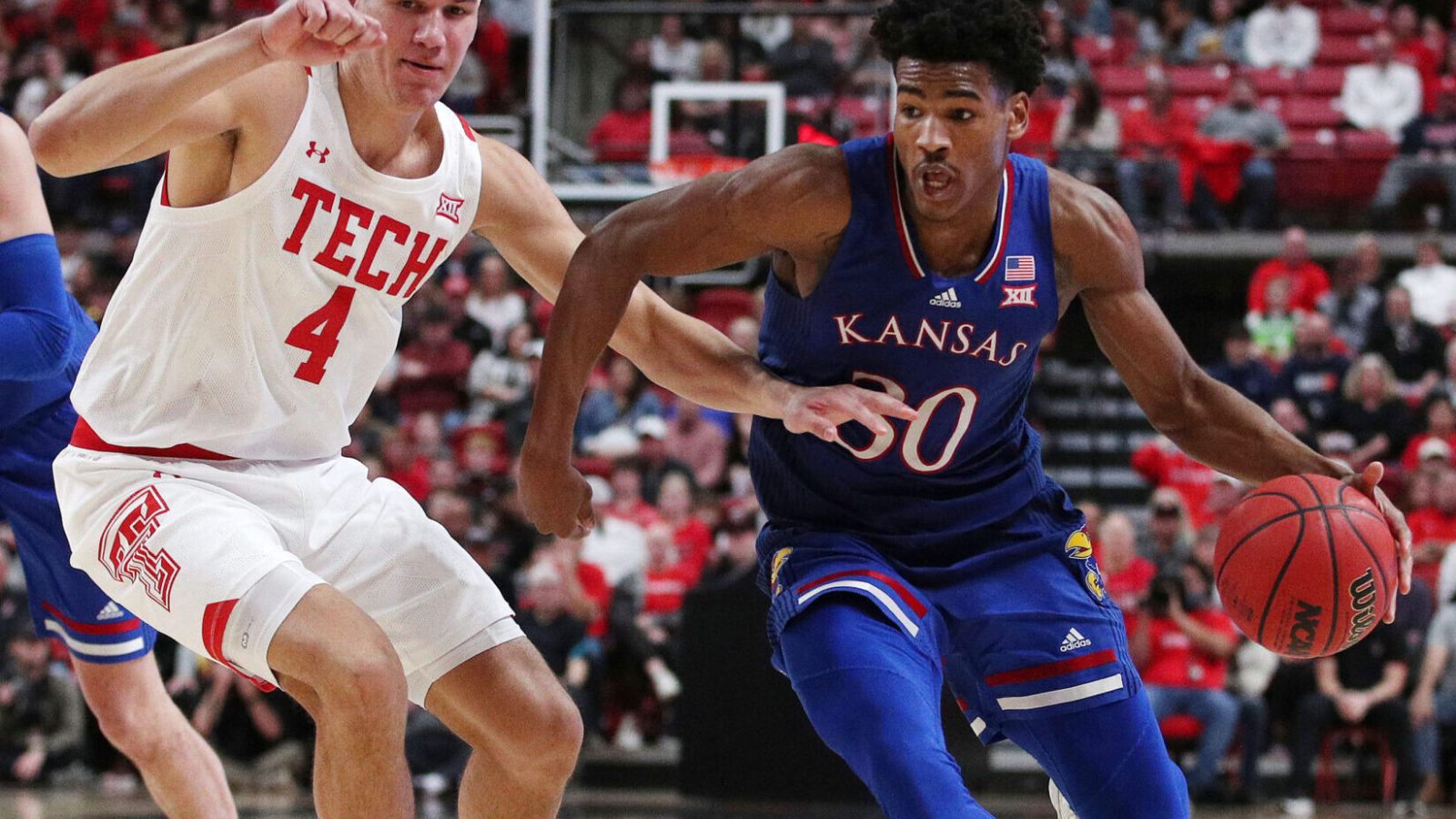 Kansas Jayhawks guard Ohai Agbaji (right) dribbles the ball with his left hand as Texas Tech Red Raiders forward Daniel Batcho (left) plays defense during a Big 12 basketball game
