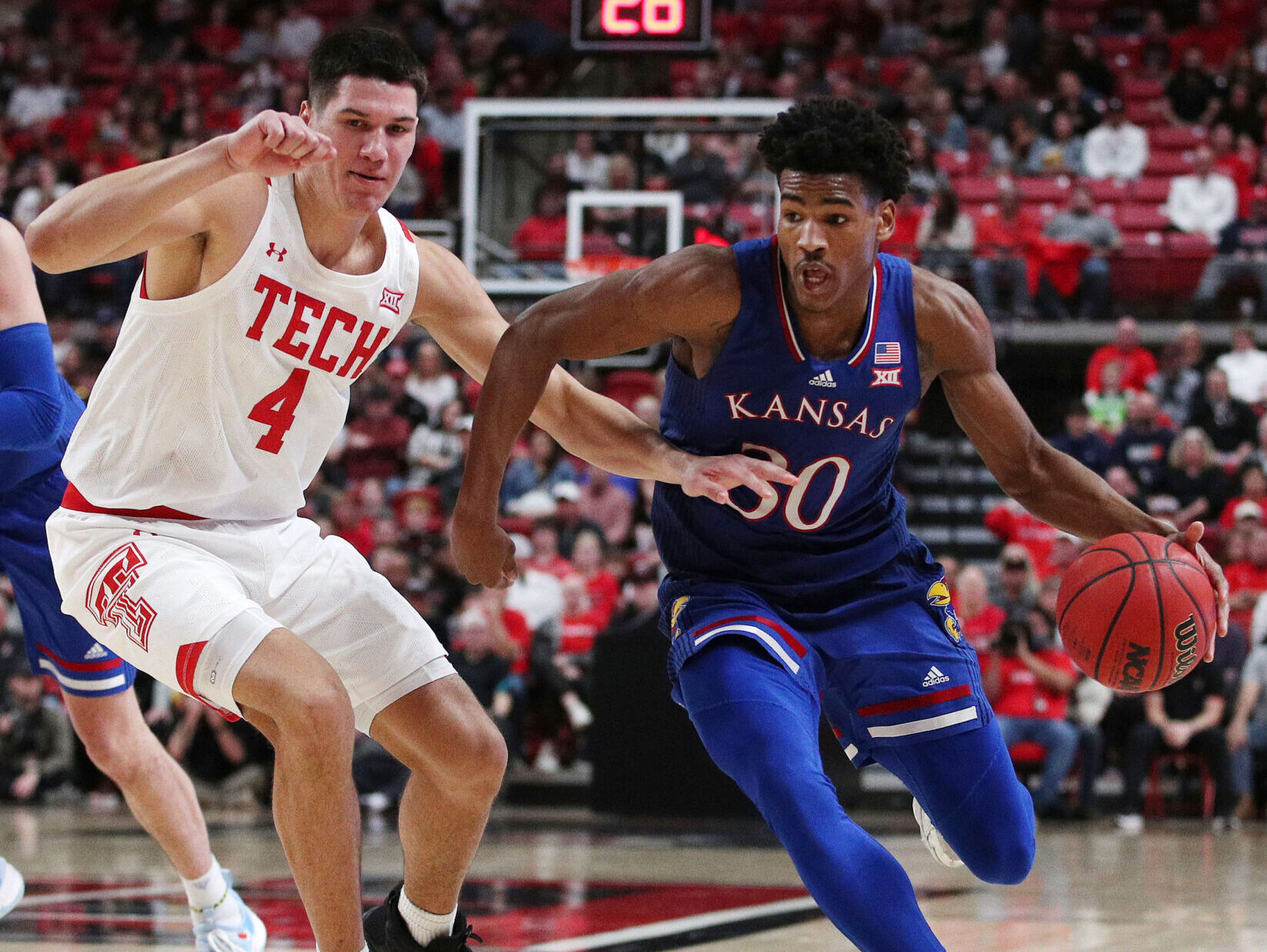 Kansas Jayhawks guard Ohai Agbaji (right) dribbles the ball with his left hand as Texas Tech Red Raiders forward Daniel Batcho (left) plays defense during a Big 12 basketball game