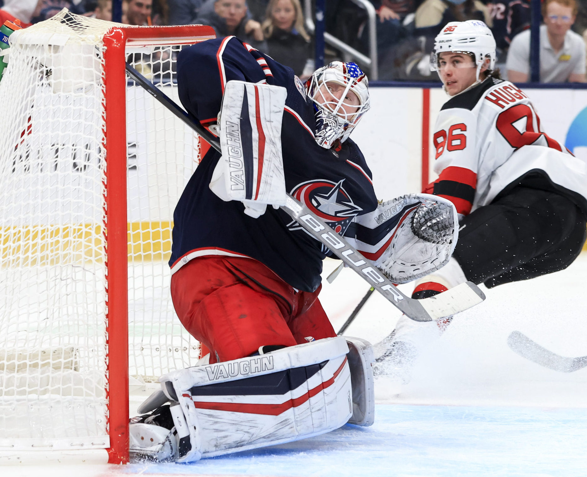 Columbus Blue Jackets goaltender Joonas Korpisalo (left) makes a save in net against New Jersey Devils shooter Jack Hughes (right)