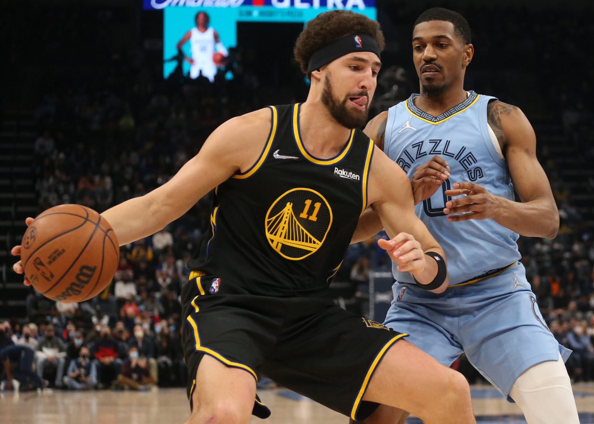 Golden State Warriors guard Klay Thompson (left) controls the basketball with his right hand and, with his tongue sticking out, tries to drive to the basket as Memphis Grizzles guard De'Anthony Melton (right) defends