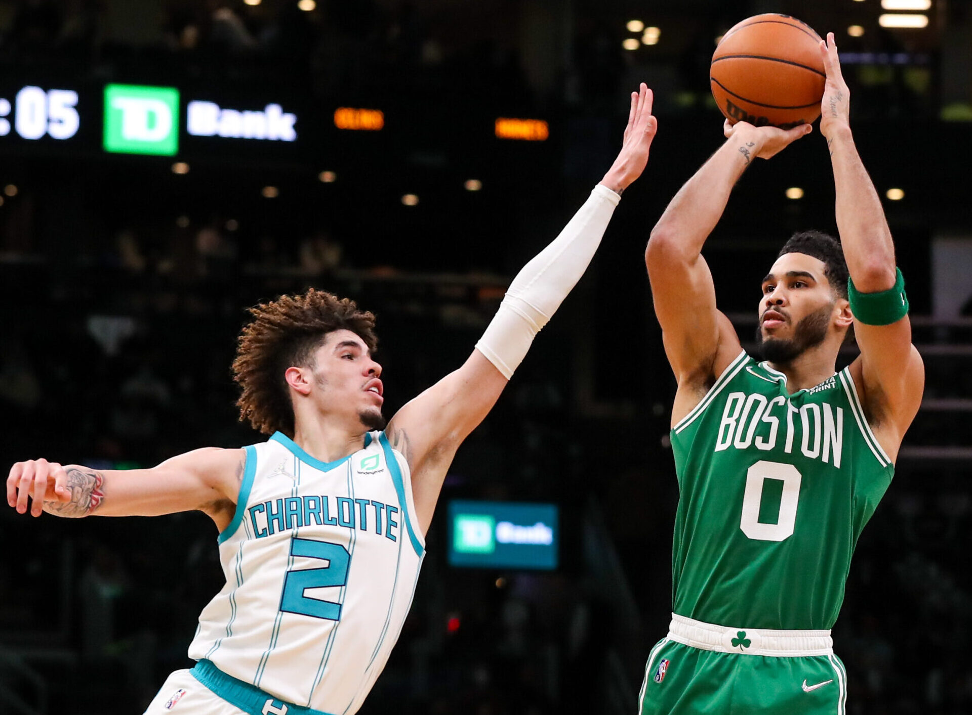 Boston Celtics forward Jayson Tatum (right) rises up and shoots a jump shot over the outstretched left hand of Charlotte Hornets defender LaMelo Ball (left)
