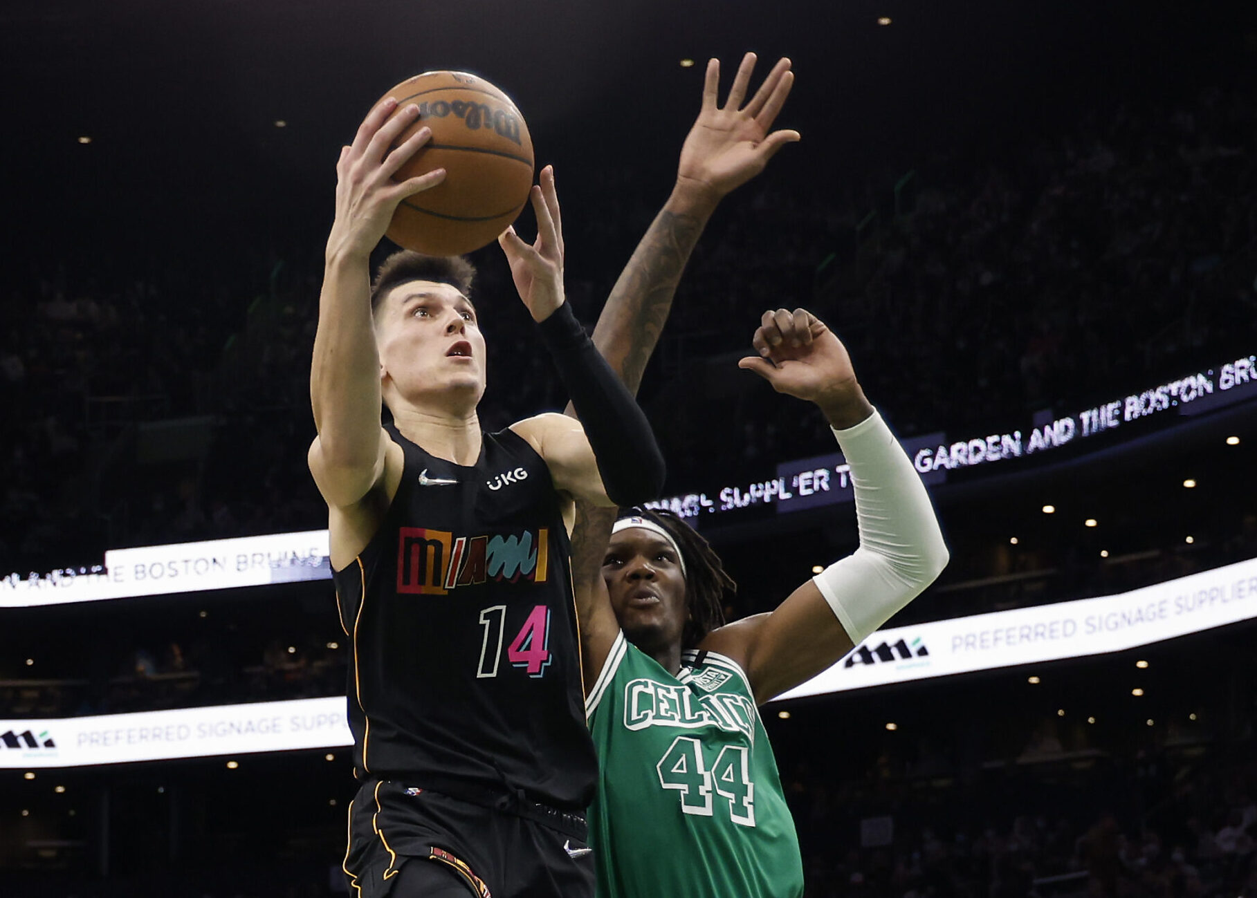 Miami Heat guard Tyler Herro (left) jumps toward the basket and prepares to shoot a layup with his right hand as Boston Celtics center Robert Williams III (right) defends with his outstretched right arm
