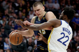 Denver Nuggets center Nikola Jokic, left, dribbles with his right hand while driving against Golden State Warriors forward Andrew Wiggins on Sunday, April 24, 2022, in Denver.