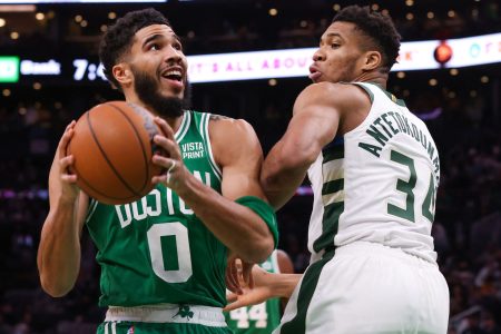Boston Celtics forward Jayson Tatum (left) controls the basketball with both hands and looks to take a shot while Milwaukee Bucks forward Giannis Antetokounmpo (right) plays tight defense