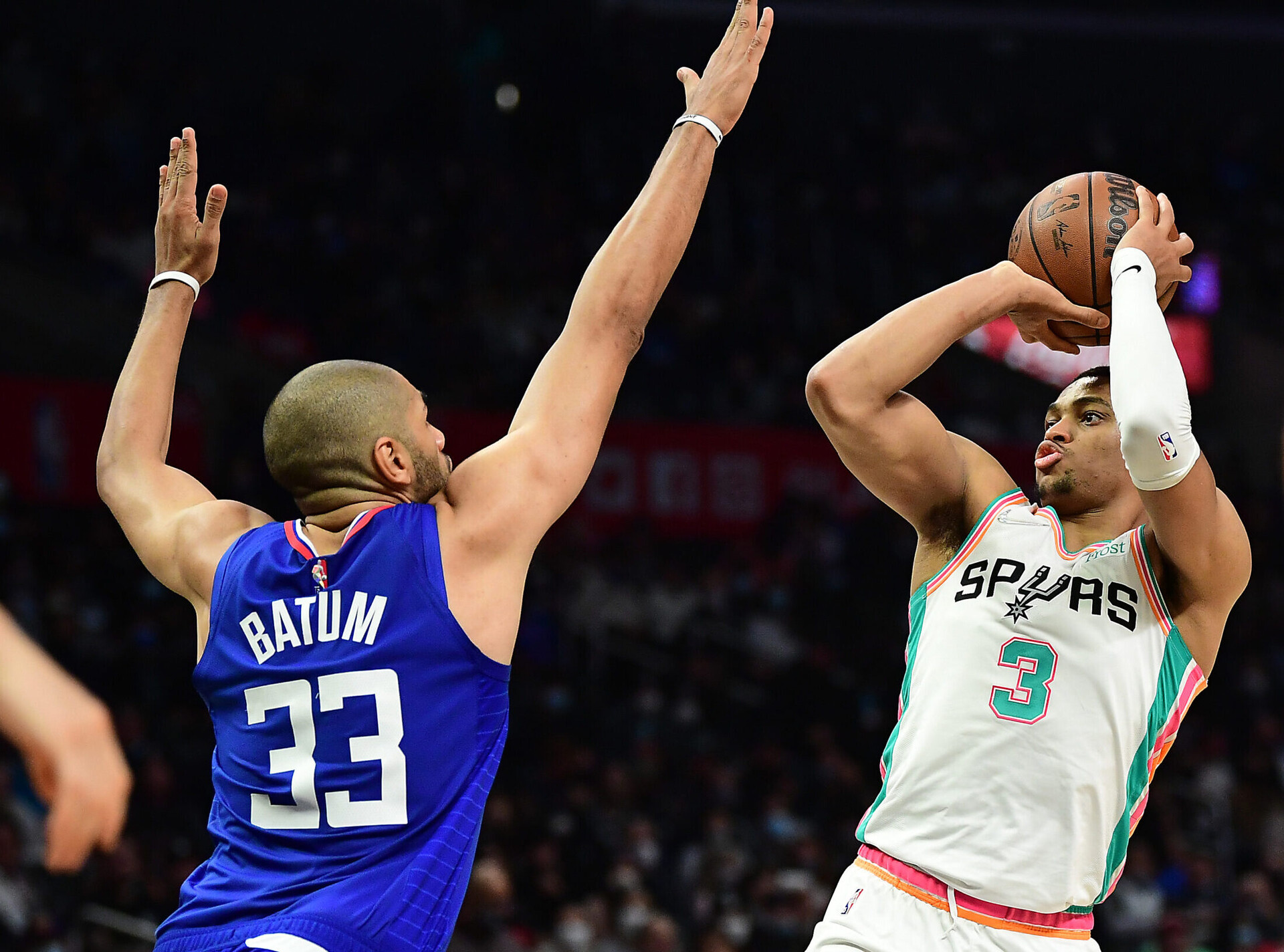 San Antonio Spurs forward Keldon Johnson (right) rises up and prepares to shoot the basketball with his right hand over the outstretched arms of defending Los Angeles Clippers forward Nicolas Batum (left)