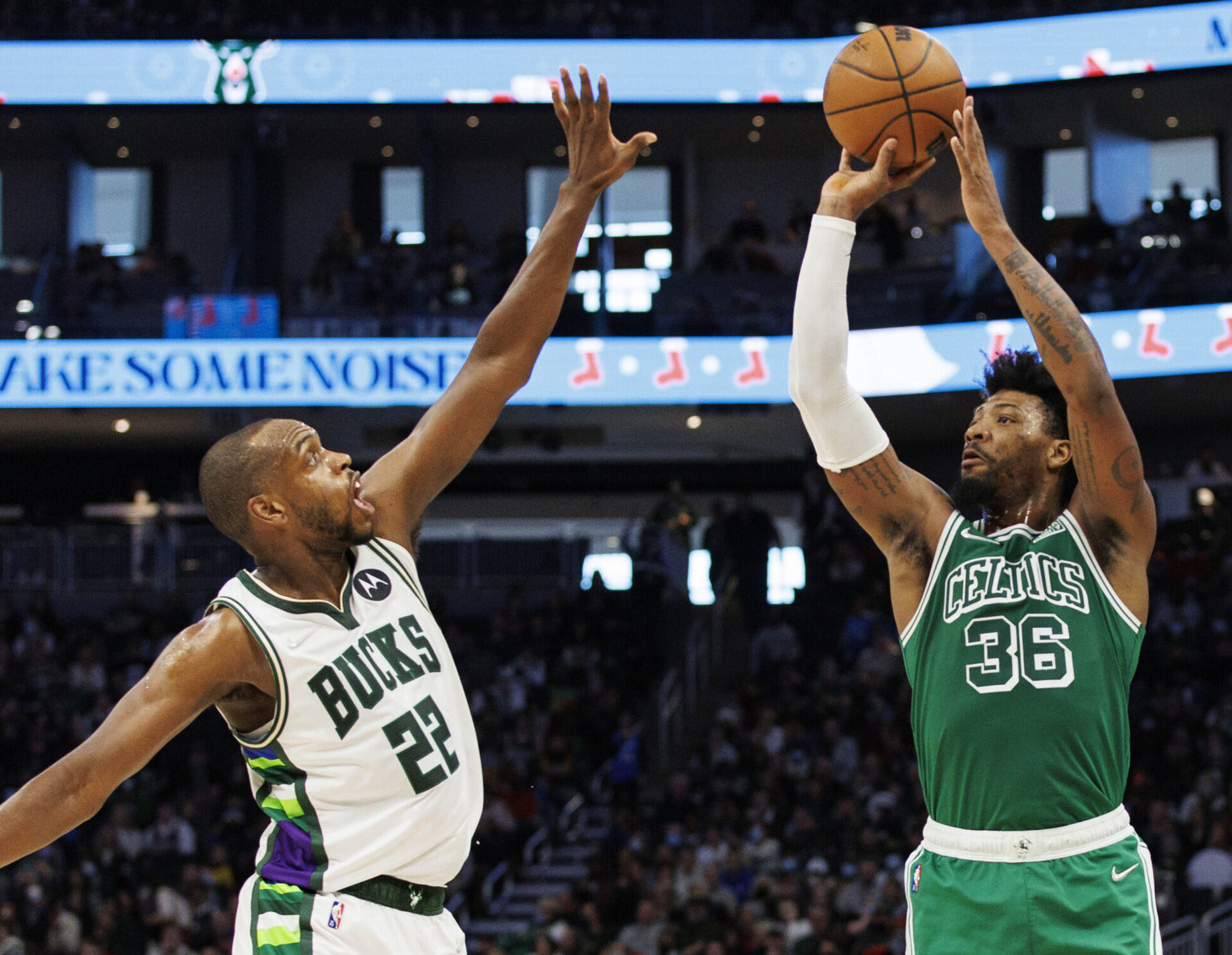 Boston Celtics guard Marcus Smart (left) rises up, extends both arms and takes a shot with his right hand over the outstretched left arm of Milwaukee Bucks forward Khris Middleton (left)