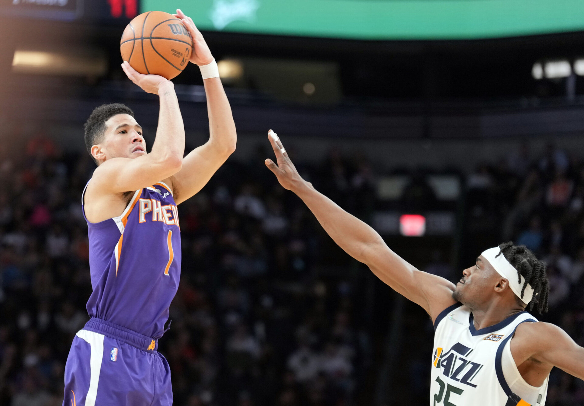 Phoenix Suns guard Devin Booker (left) rises up and prepares to shoot the basketball with his right hand over the outstretched right arm of Utah Jazz forward Danuel House Jr (right)