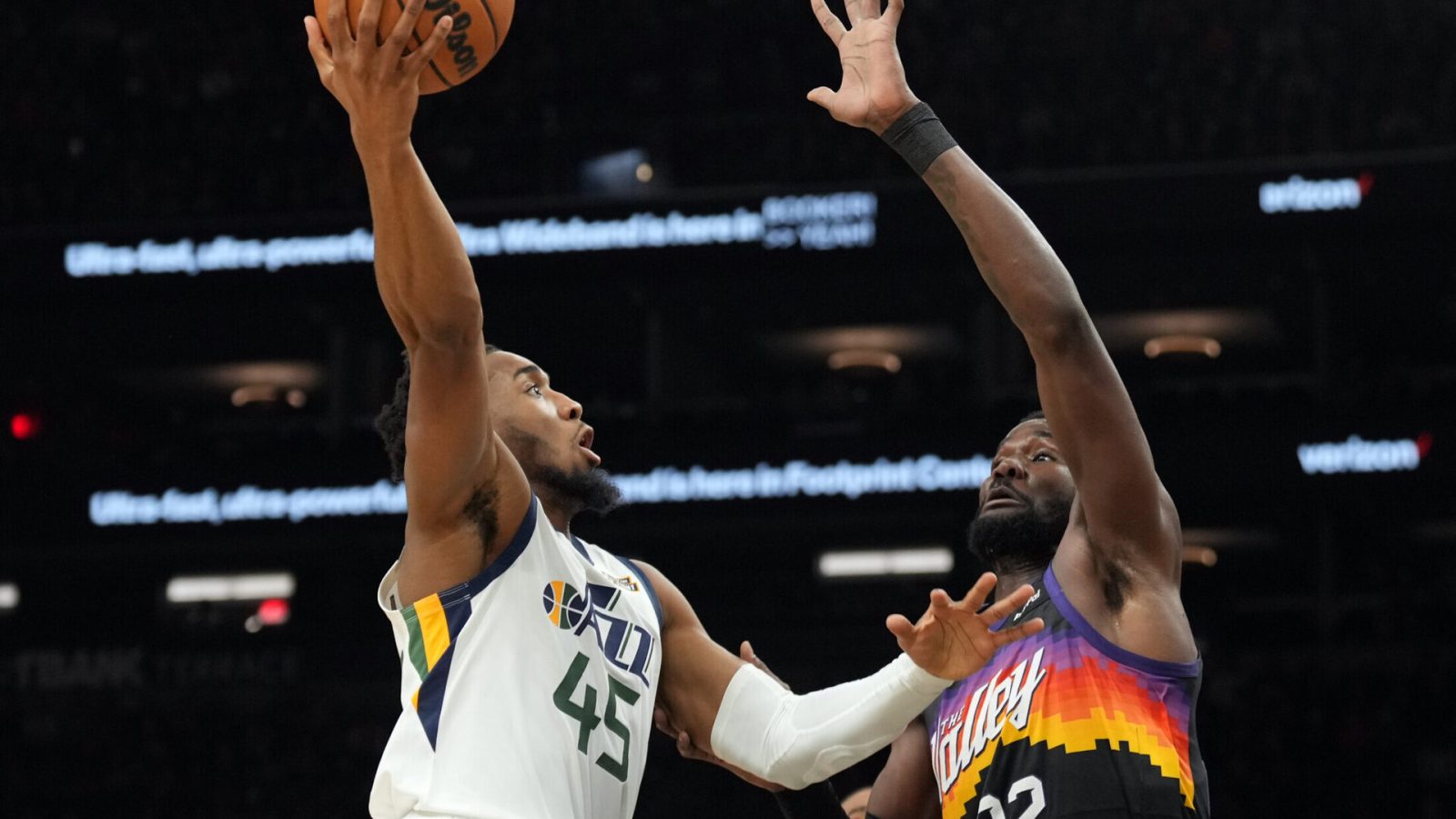Utah Jazz guard Donovan Mitchell (left) jumps in the air and prepares to shoot a right-handed hook shot over the outstretched left arm of Phoenix Suns center Deandre Ayton (right)