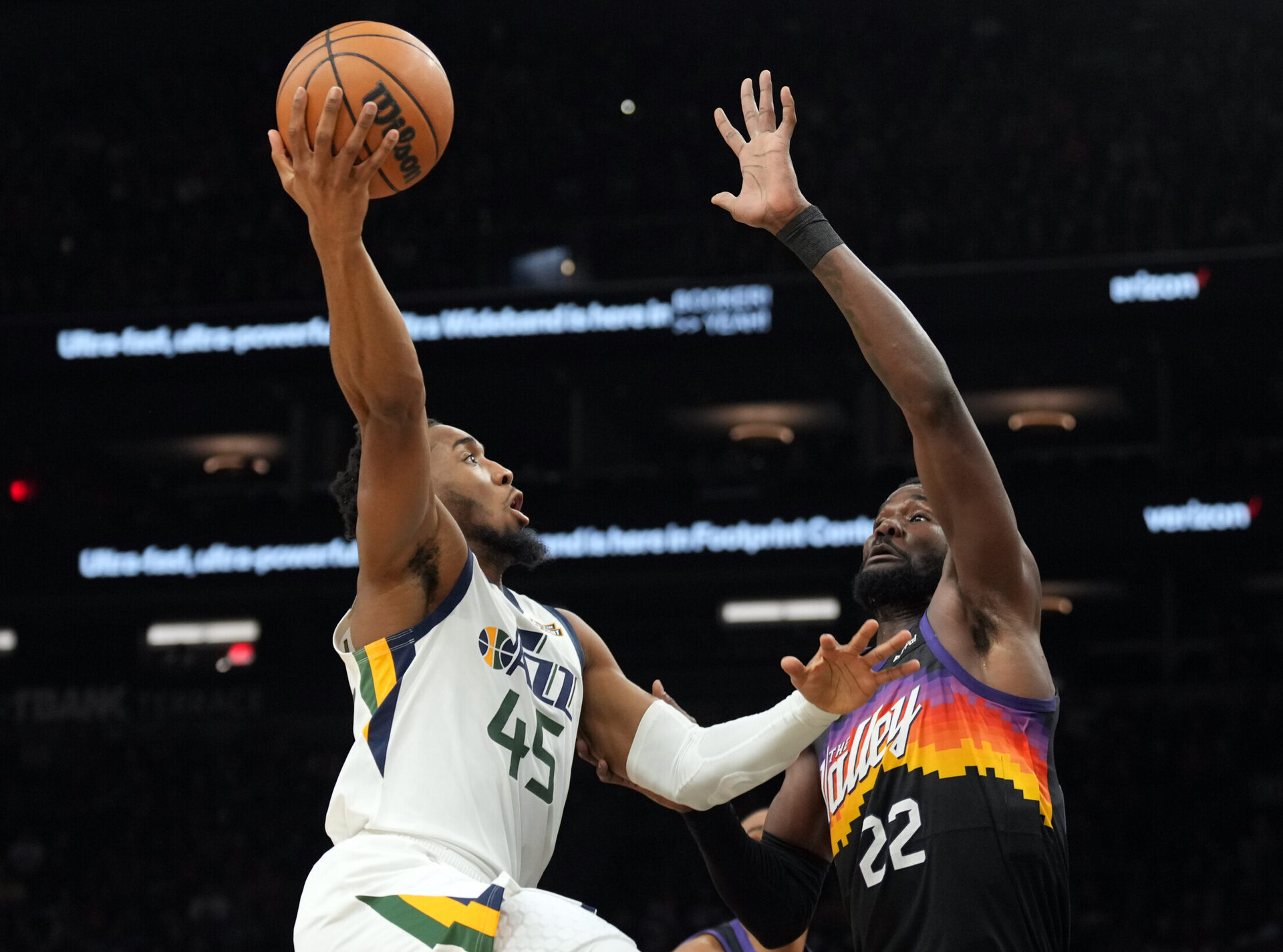 Utah Jazz guard Donovan Mitchell (left) jumps in the air and prepares to shoot a right-handed hook shot over the outstretched left arm of Phoenix Suns center Deandre Ayton (right)