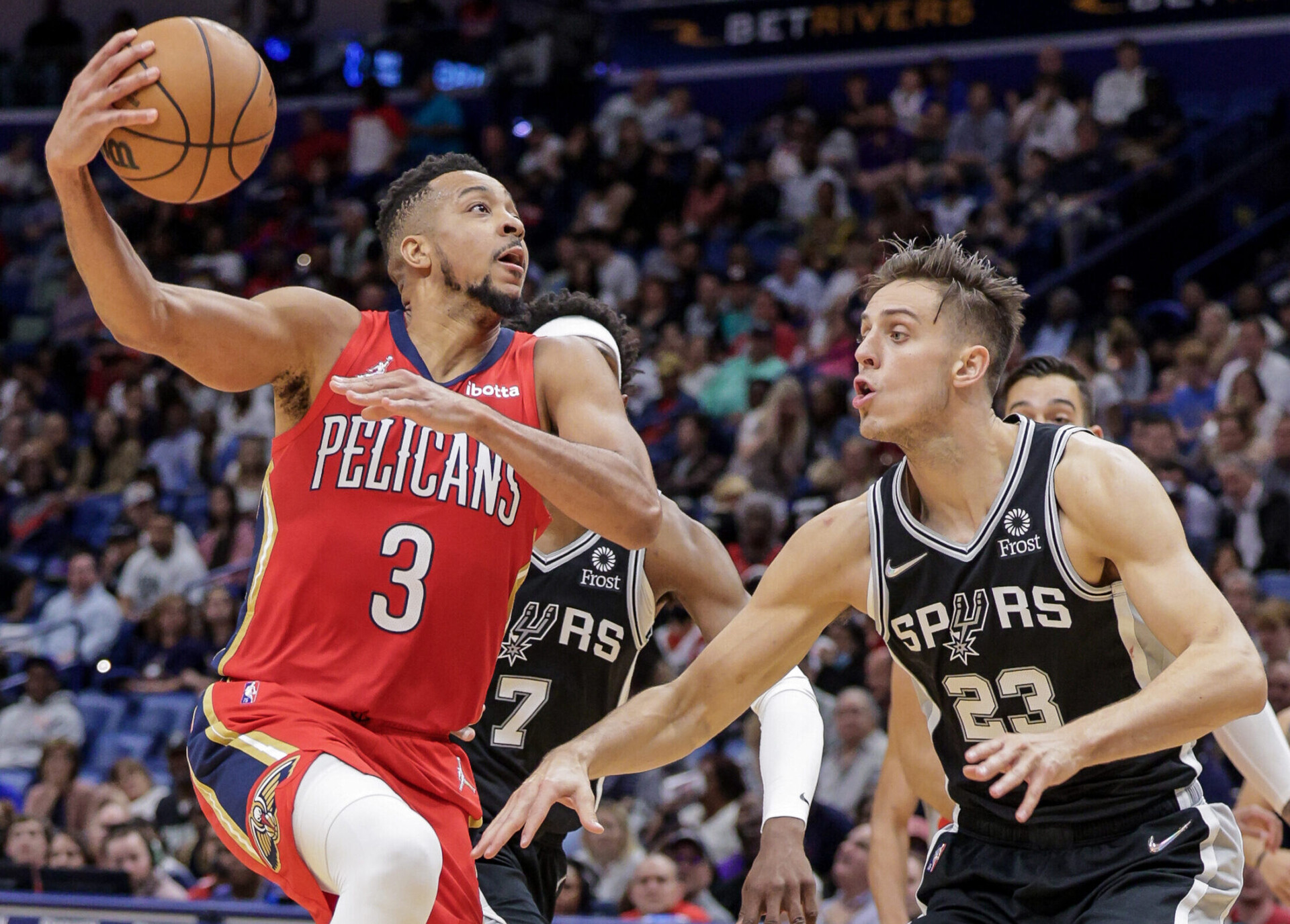 New Orleans Pelicans guard CJ McCollum (left) drives to the basket and rises up to shoot a layout with his right hand as San San Antonio Spurs forward Zach Collins (left) defends