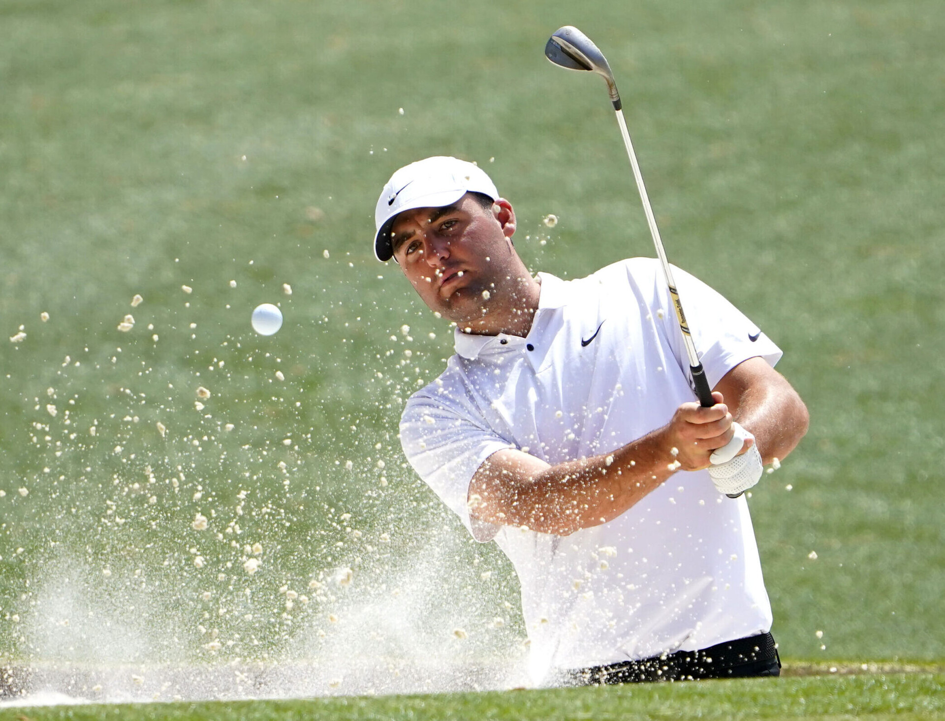 PGA Tour player Scottie Scheffler follows through on his golf swing after hitting out of a bunker on the 16th hole during a practice round of The Masters golf tournament
