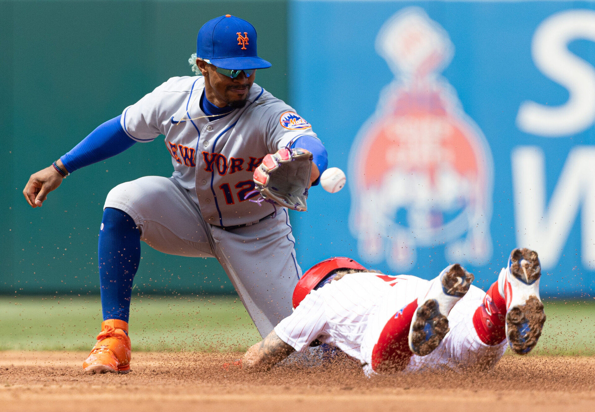 Philadelphia Phillies shortstop Bryson Stott (right) dives head first into second base as New York Mets shortstop Francisco Lindor (left) prepares to catch the ball with is left hand and tag out Stott, who attempted to stretch a single into a double