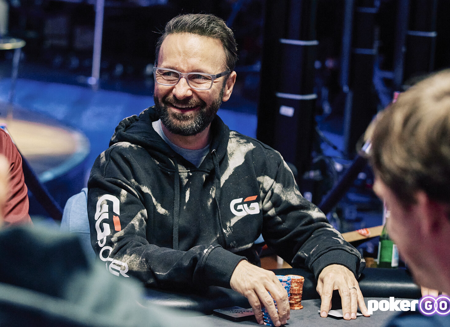 Daniel Negreanu smiles while holding chips and cards during a PokerGO Cup event at the PokerGO studio in Las Vegas in 2021.