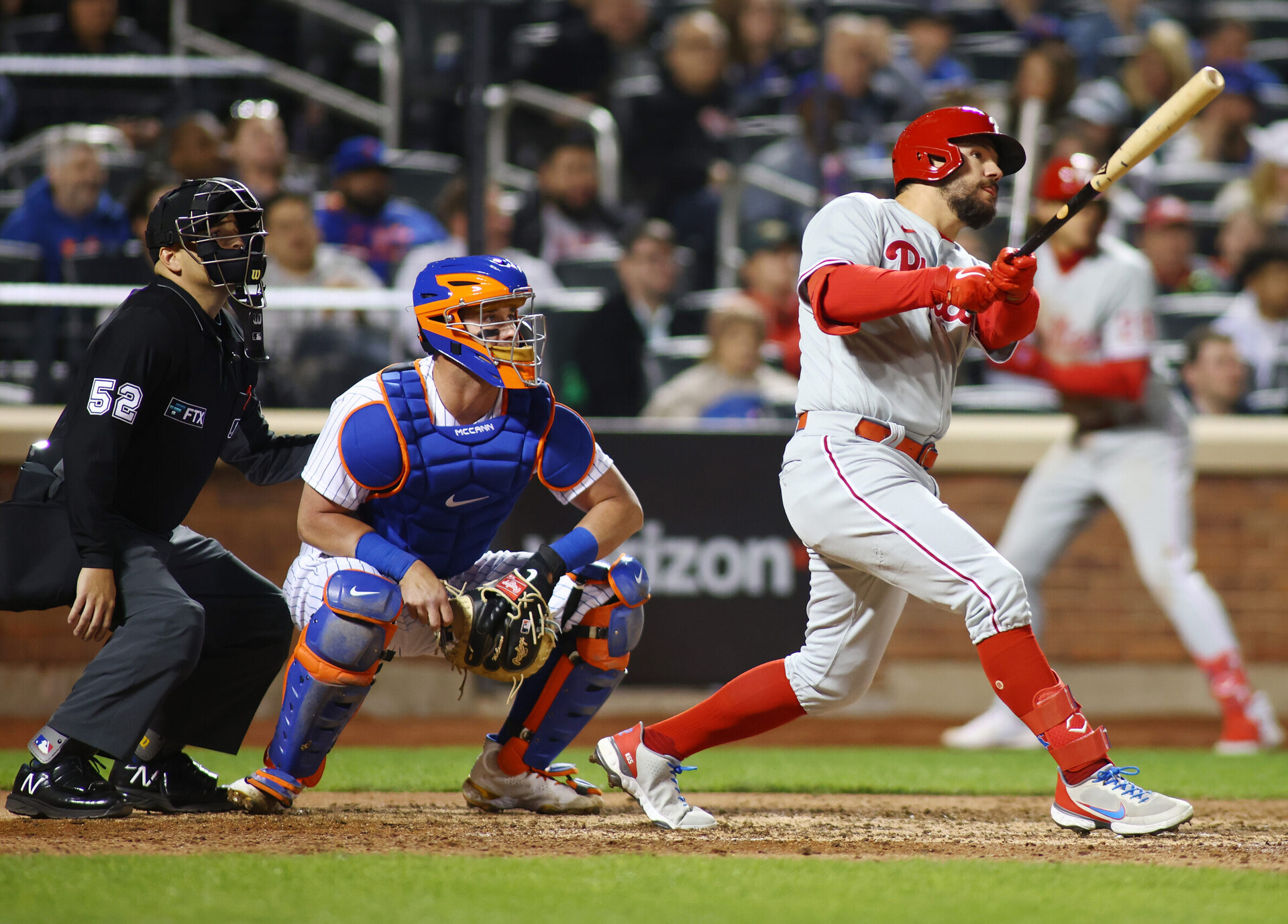Philadelphia Phillies outfielder Kyle Schwarber, right, hits a two-run home run as New York Mets catcher James McCann, center, and the umpire watch on Saturday, April 30, 2022, in New York.