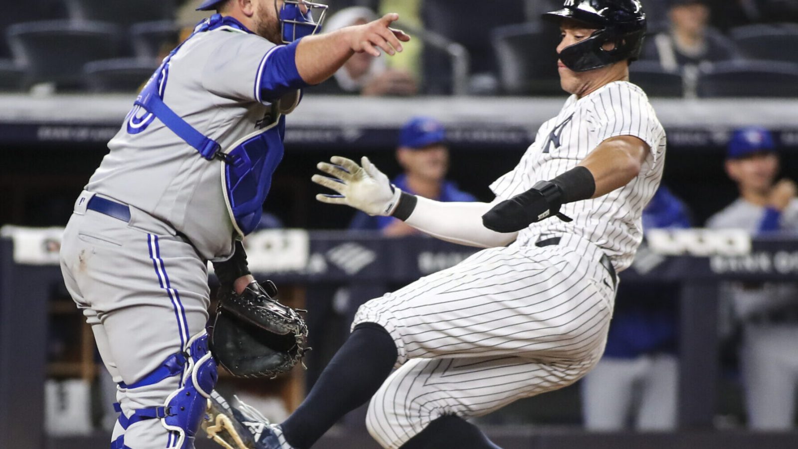 New York Yankees right fielder Aaron Judge (right) slides safely into a home plate as an unidentified Toronto Blue Jays catcher (left) directs his infield where to throw the ball