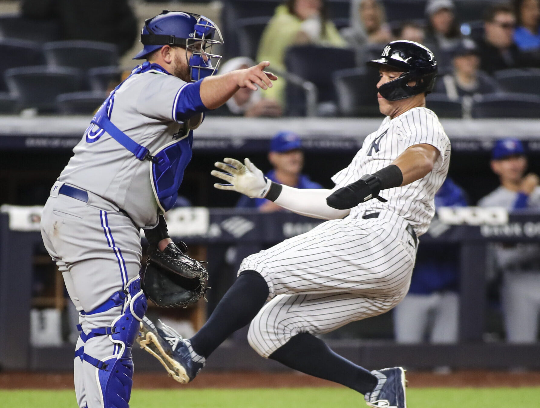 New York Yankees right fielder Aaron Judge (right) slides safely into a home plate as an unidentified Toronto Blue Jays catcher (left) directs his infield where to throw the ball
