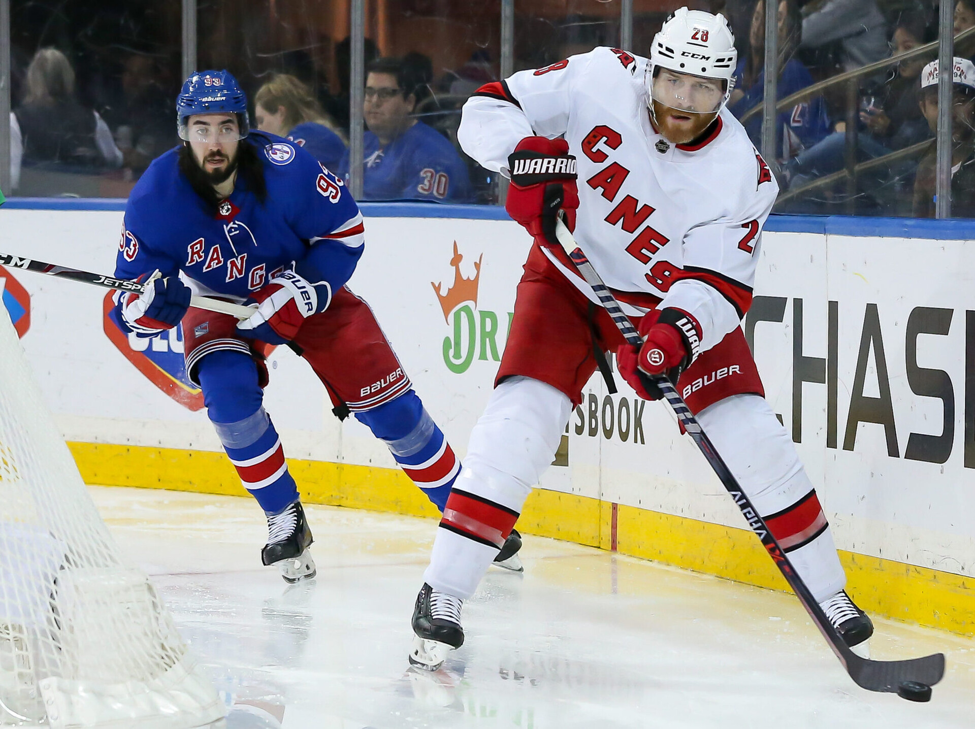 Carolina Hurricanes defenseman Ian Cole (right, foreground) moves the puck past trailing New York Rangers center Mika Zibanejad (left)