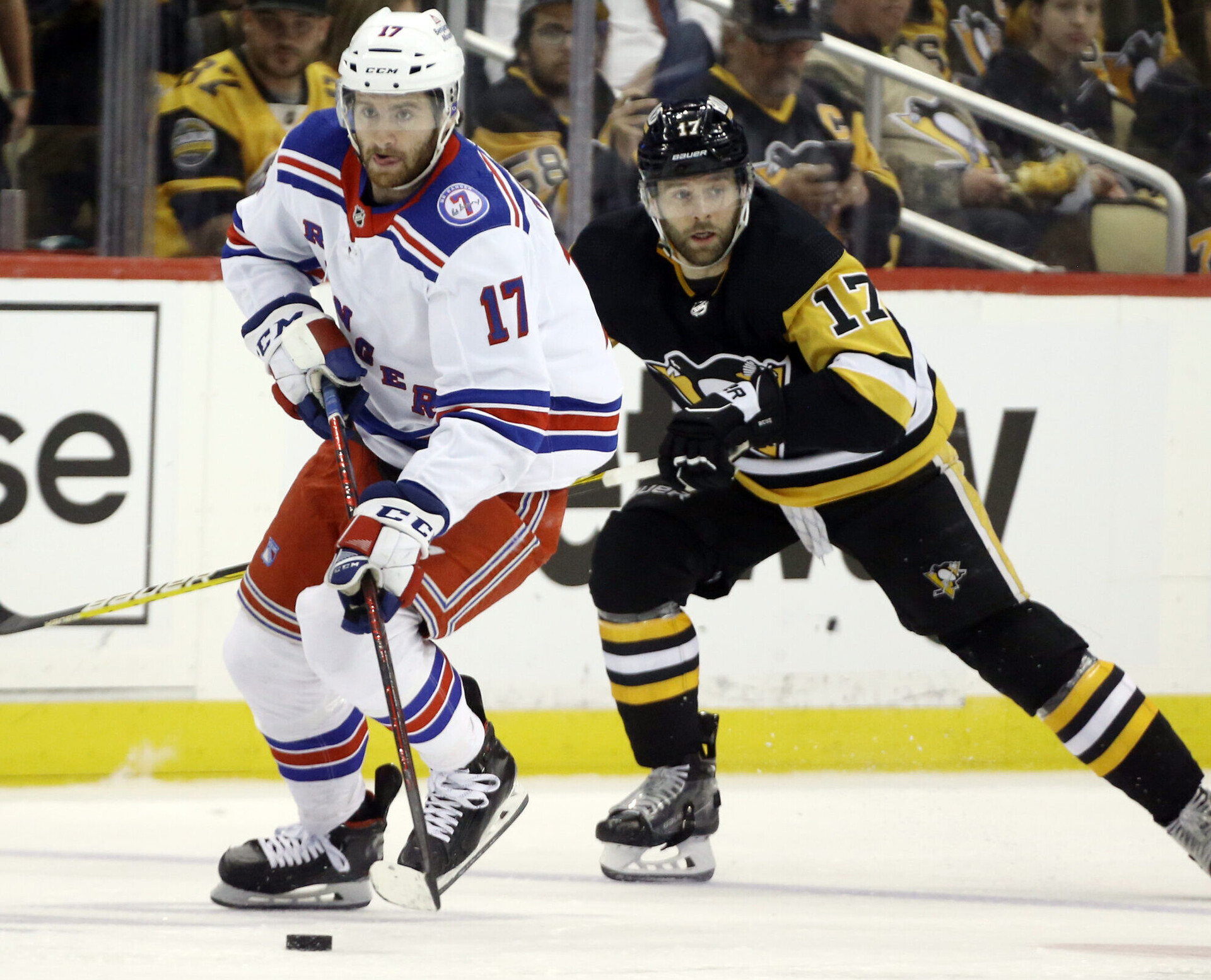 New York Rangers center Kevin Rooney (left) skates with the puck while Pittsburgh Penguins right wing Bryan Rust pursues from behind during a 2022 Stanley Cup Playoffs game