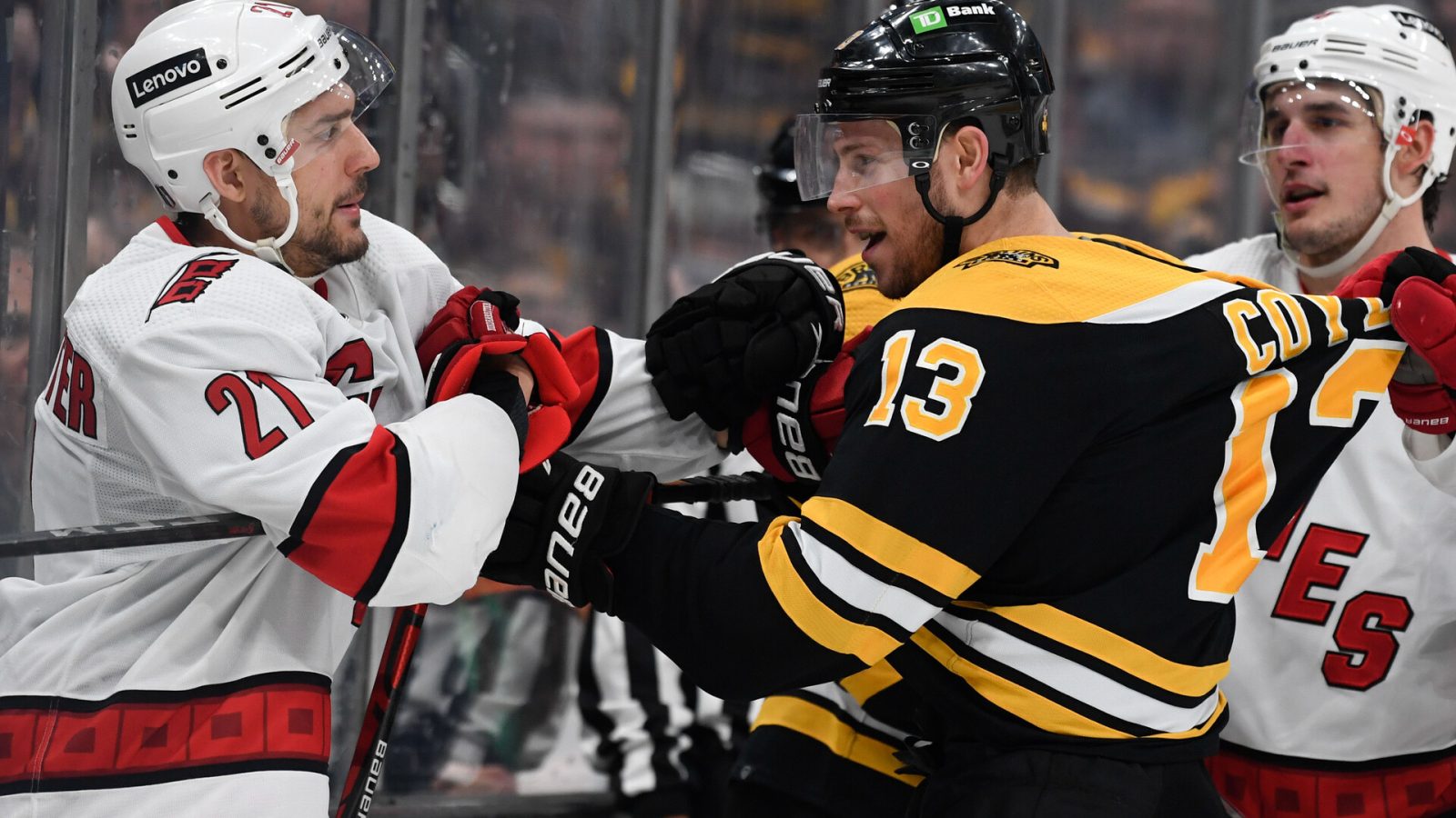 Boston Bruins center Charlie Coyle (center) shoves Carolina Hurricanes right wing Nino Niederreiter (left) after a whistle during a 2022 Stanley Cup Playoffs game. An unidentified Carolina player (right) yanks on Coyle's jersey