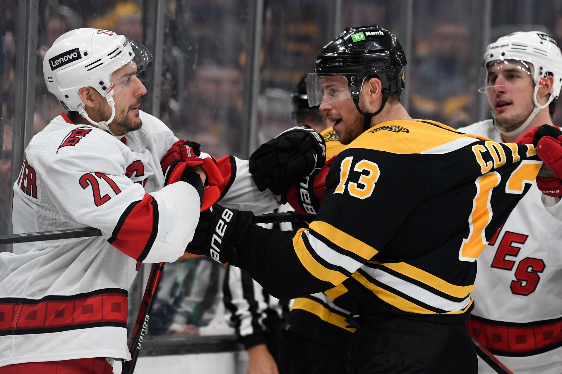 Boston Bruins center Charlie Coyle (center) shoves Carolina Hurricanes right wing Nino Niederreiter (left) after a whistle during a 2022 Stanley Cup Playoffs game. An unidentified Carolina player (right) yanks on Coyle's jersey