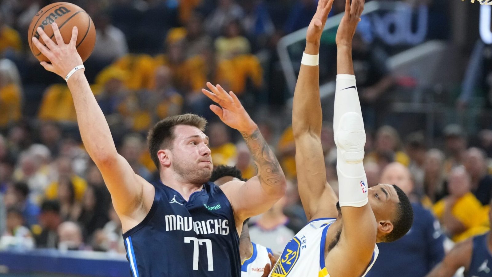 Dallas Mavericks guard Luka Doncic, left, throws a no-look pass behind his back with his right hand while being guarded by Golden State Warriors forward Otto Porter Jr., right with hands in the air, on Friday, May 20, 2022, in San Francisco.