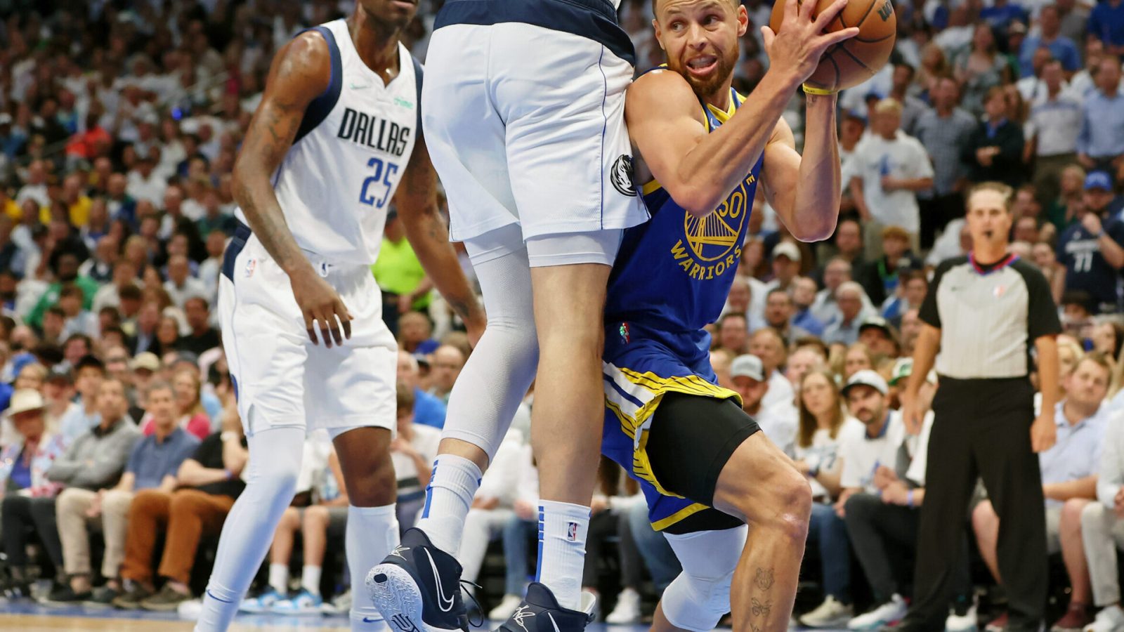 Golden State Warriors guard Stephen Curry, right, looks for an opening around leaping Dallas Mavericks forward Maxi Kleber, top of body out of frame, while Mavericks forward Reggie Bullock, left, watches on Tuesday, May 24, 2022, in Dallas.