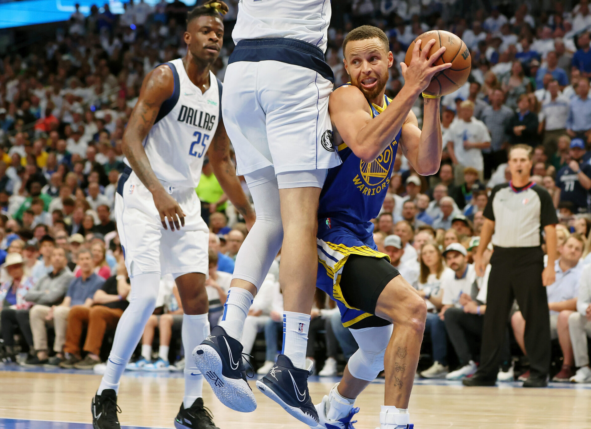 Golden State Warriors guard Stephen Curry, right, looks for an opening around leaping Dallas Mavericks forward Maxi Kleber, top of body out of frame, while Mavericks forward Reggie Bullock, left, watches on Tuesday, May 24, 2022, in Dallas.