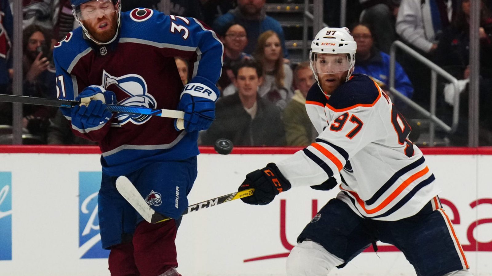 Colorado Avalanche left wing J.T. Compher (left) and Edmonton Oilers center Connor McDavid (right) swing their sticks at an elevated puck during the second period in Game 1 of the 2022 NHL Western Conference Finals
