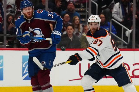 Colorado Avalanche left wing J.T. Compher (left) and Edmonton Oilers center Connor McDavid (right) swing their sticks at an elevated puck during the second period in Game 1 of the 2022 NHL Western Conference Finals