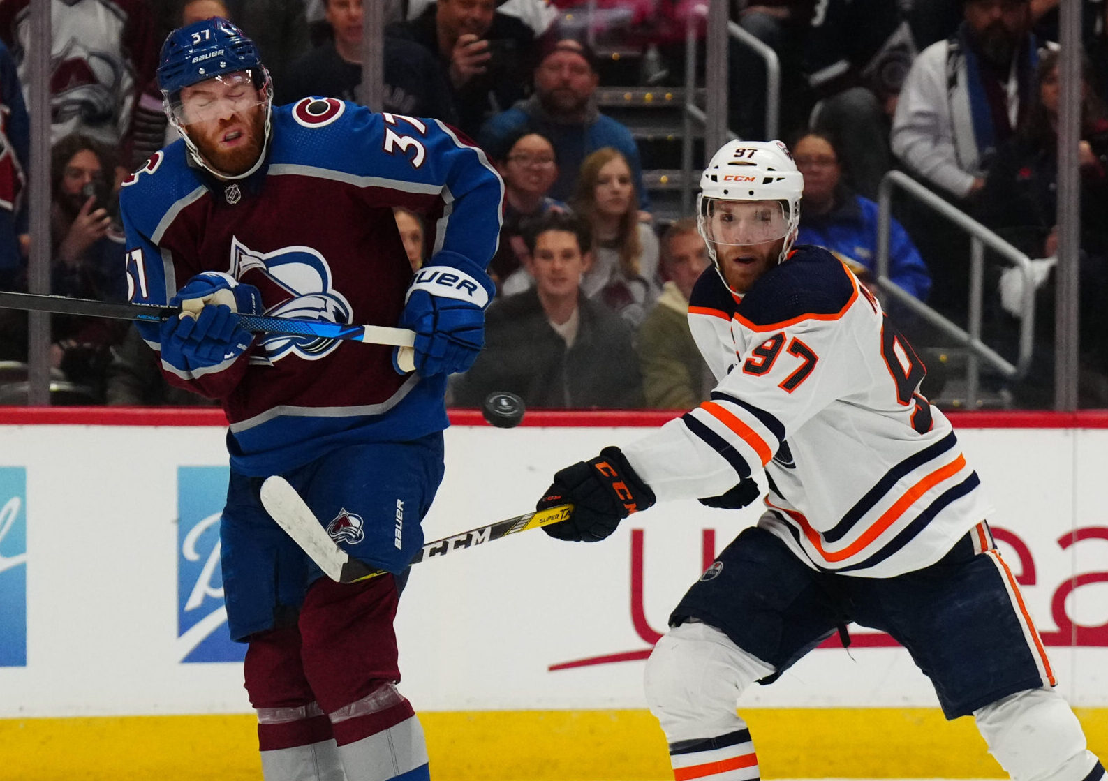 Colorado Avalanche left wing J.T. Compher (left) and Edmonton Oilers center Connor McDavid (right) swing their sticks at an elevated puck during the second period in Game 1 of the 2022 NHL Western Conference Finals