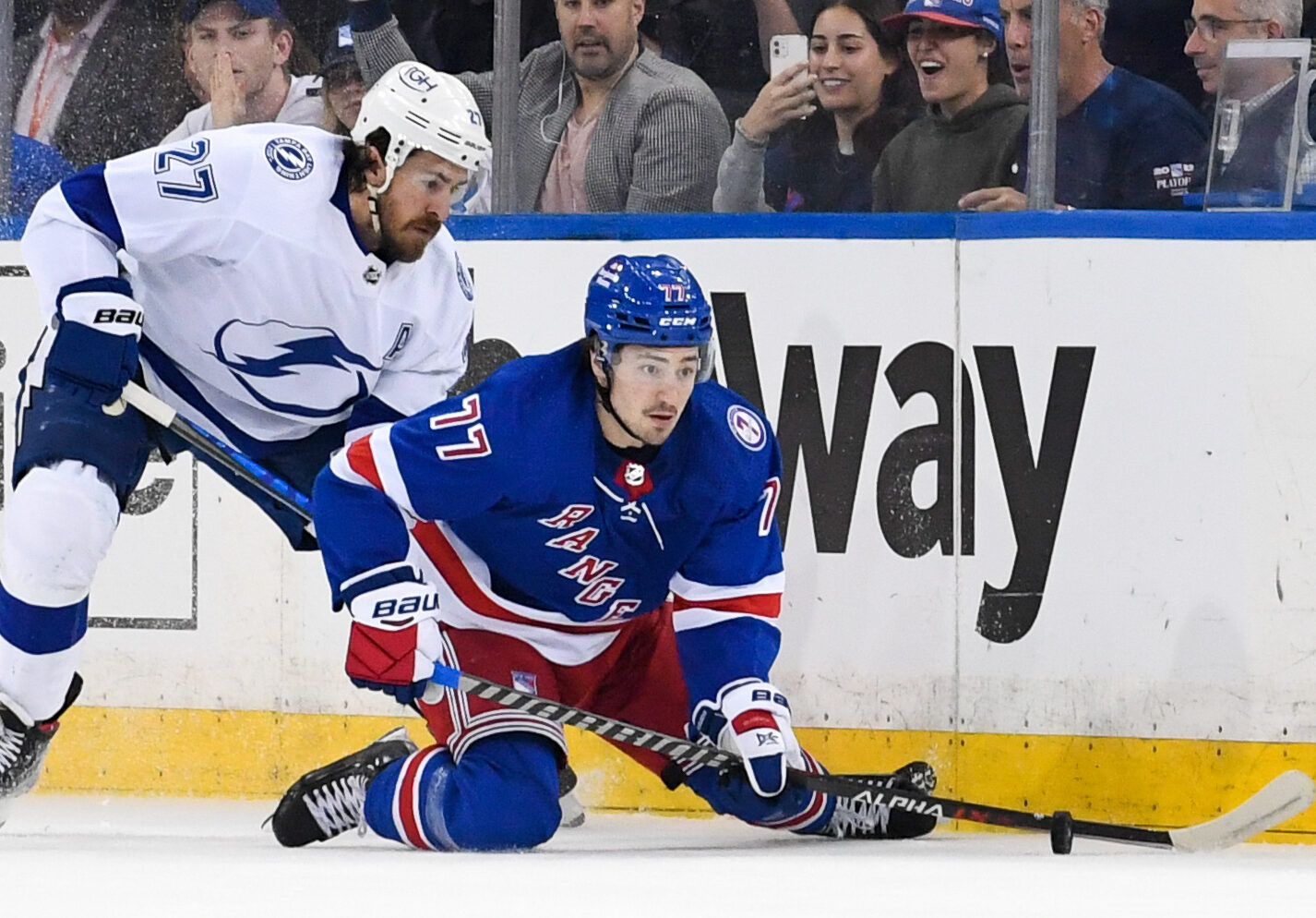 New York Rangers center Frank Vatrano (right) plays the puck with his stick while on his knees as Tampa Bay Lightning defenseman Ryan McDonagh (left) applies pressure from behind during Game 2 of the Eastern Conference Finals of the 2022 Stanley Cup Playoffs