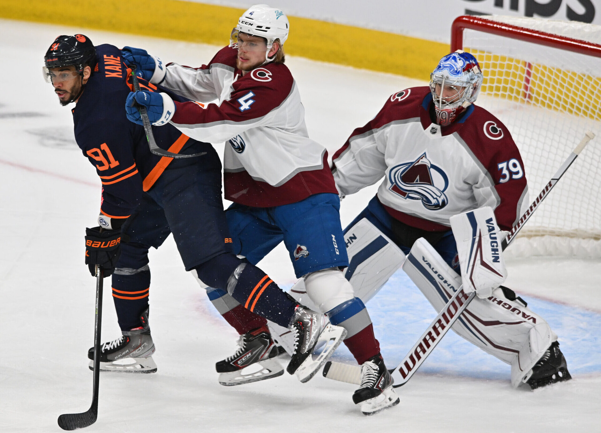 Colorado Avalanche defenseman Bowen Byram (center) shoves his stick into the upper back of Edmonton Oilers left wing Evander Kane (left) as the two battle for position in front of Colorado goaltender Pavel Francouz (right) during Game 3 of the Western Conference Finals of the 2022 Stanley Cup Playoffs