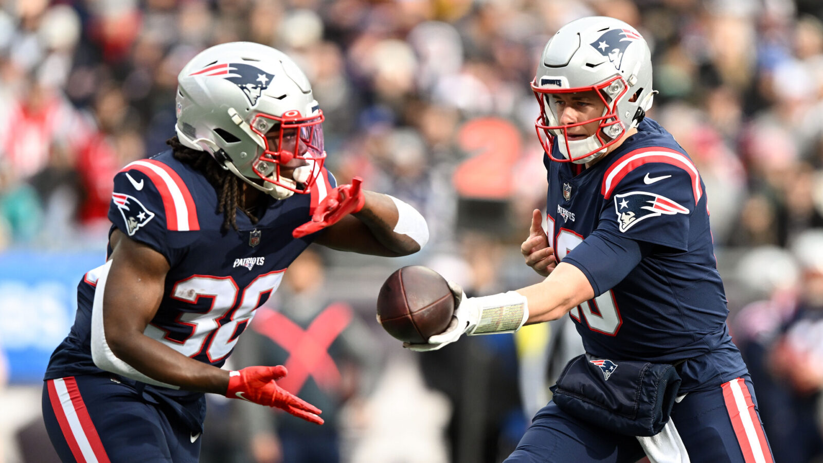 Jan 1, 2023; Foxborough, Massachusetts, USA; New England Patriots quarterback Mac Jones (10) hands the ball to running back Rhamondre Stevenson (38) during the first half of a game against the Miami Dolphins at Gillette Stadium.