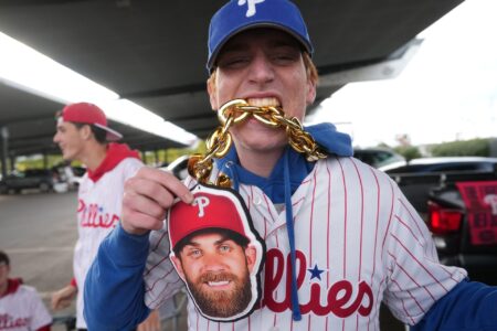 Sean McIvor takes a bite of his Bryce Harper chain at Citizens Bank Park before the gates open on their NLCS game against the Arizona Diamondbacks at Citizens Bank Park in Philadelphia on Oct. 16, 2023.