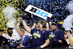 Aidan Hutchinson #97 of the Michigan Wolverines celebrates with the trophy after the Michigan Wolverines beat the Iowa Hawkeyes 42-3 to win the Big Ten Championship game at Lucas Oil Stadium on December 04, 2021 in Indianapolis, Indiana.