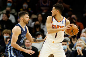 Devin Booker #1 of the Phoenix Suns looks to pass around John Konchar #46 of the Memphis Grizzlies during the NBA game at Footprint Center on December 27, 2021 in Phoenix, Arizona. The Grizzlies defeated the Suns 114-113.