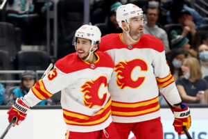 Johnny Gaudreau #13 of the Calgary Flames celebrates his goal with Erik Gudbranson #44 and Matthew Tkachuk #19 during the first period against the Seattle Kraken at Climate Pledge Arena on December 30, 2021 in Seattle, Washington.