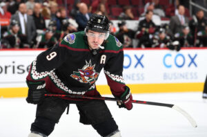 Arizona Coyotes player Clayton Keller chews on his mouthpiece while awaiting a faceoff during a game against the Dallas Stars