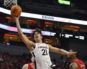 Virginia Cavaliers forward Kadin Shedrick (center) takes the basketball to the rim with his right hand as Louisville Cardinals forward Malik Williams (right) looks on during an ACC basketball game